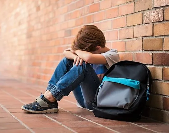 Jeune garçon triste assis par terre avec son sac à dos. Accompagnement thérapeutique par le jeu à Nantes pour aider les enfants à désamorcer le harcèlement scolaire.